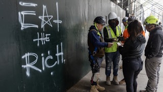 Construction workers settle their lunch bills next to graffiti scrawled on the wall of a construction site reading "eat the rich" in New York City.