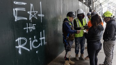 Construction workers settle their lunch bills next to graffiti scrawled on the wall of a construction site reading "eat the rich" in New York City.