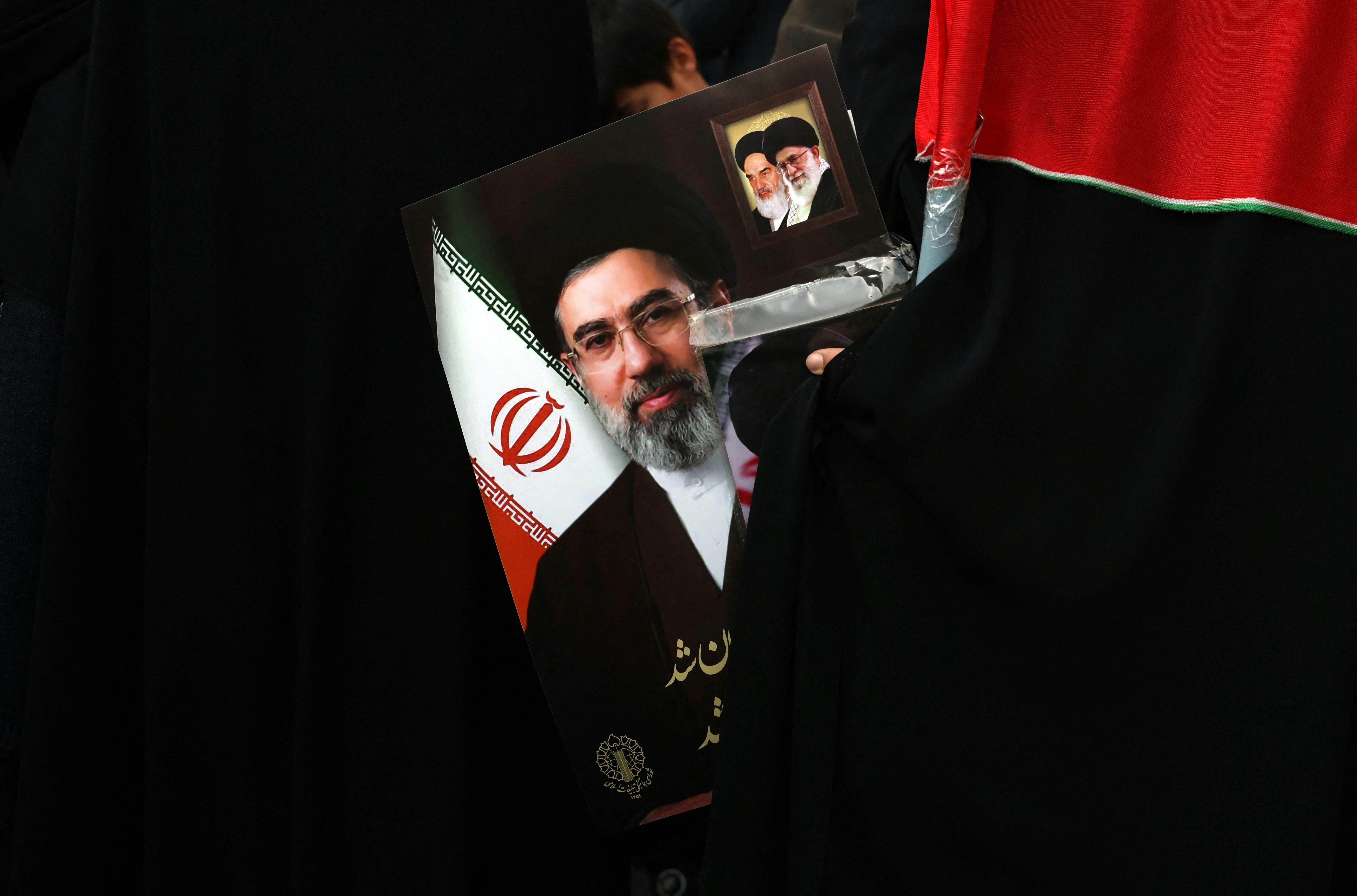 A demonstrator holds a picture of Iran’s new Supreme Leader Ayatollah Mojtaba Khamenei. The poster includes smaller photos of Ali Khamenei and Ruhollah Khomeini.