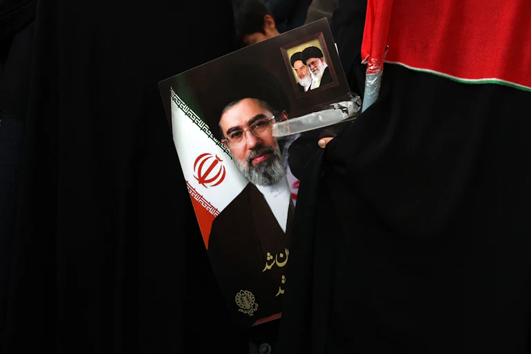 A demonstrator holds a picture of Iran’s new Supreme Leader Mojtaba Khamenei. The poster includes smaller photos of Ali Khamenei and Ruhollah Khomeini.