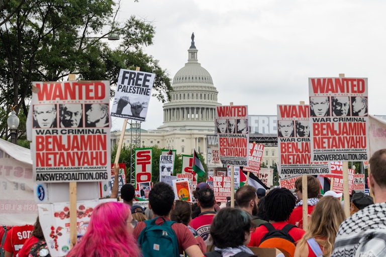 Pro-Palestine protesters march toward the Capitol with signs that call Benjamin Netanyahu a war criminal or read "Free Palestine."