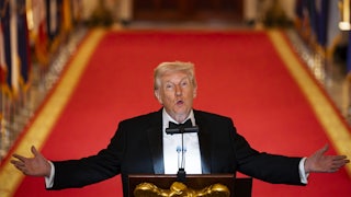 Donald Trump holds his arms out to the side and looks up while speaking at a podium