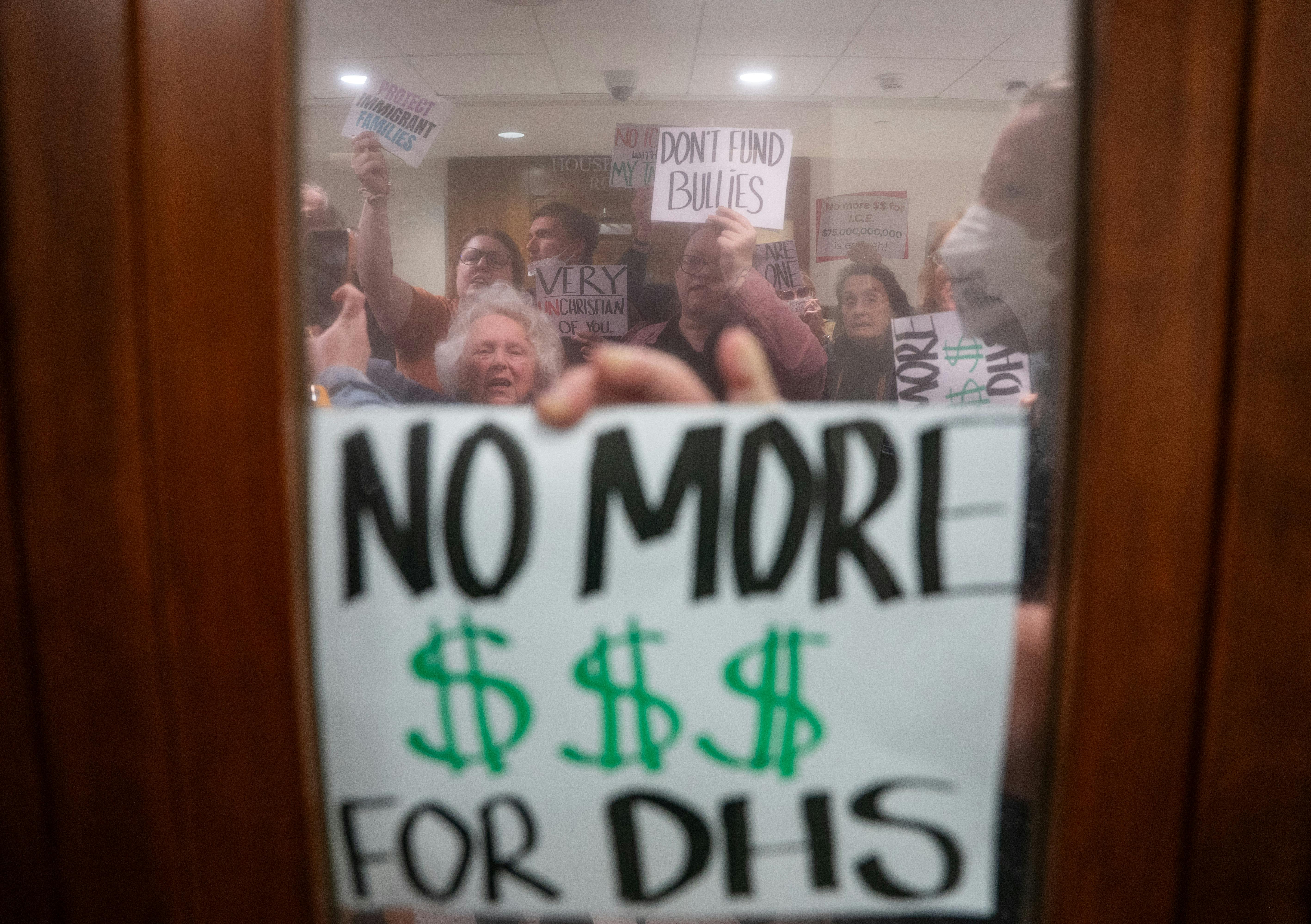 A person holds a sign that says, "No more $$$ for DHS" up to a window during an anti-ICE protest in Nashville, Tennessee