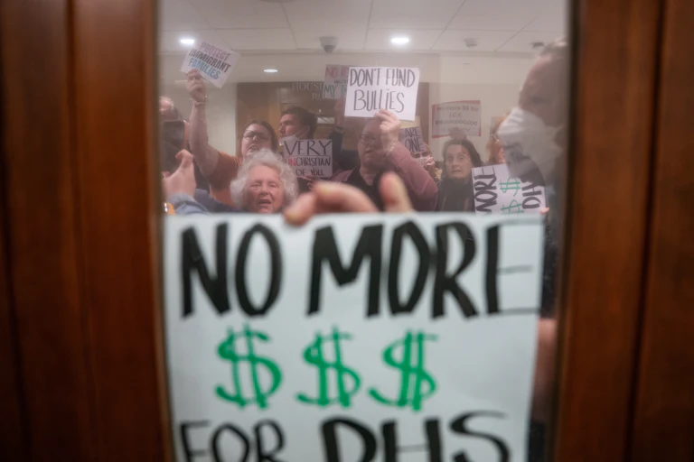 A person holds a sign that says, "No more $$$ for DHS" up to a window during an anti-ICE protest in Nashville, Tennessee