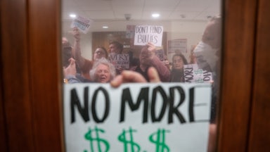 A person holds a sign that says, "No more $$$ for DHS" up to a window during an anti-ICE protest in Nashville, Tennessee