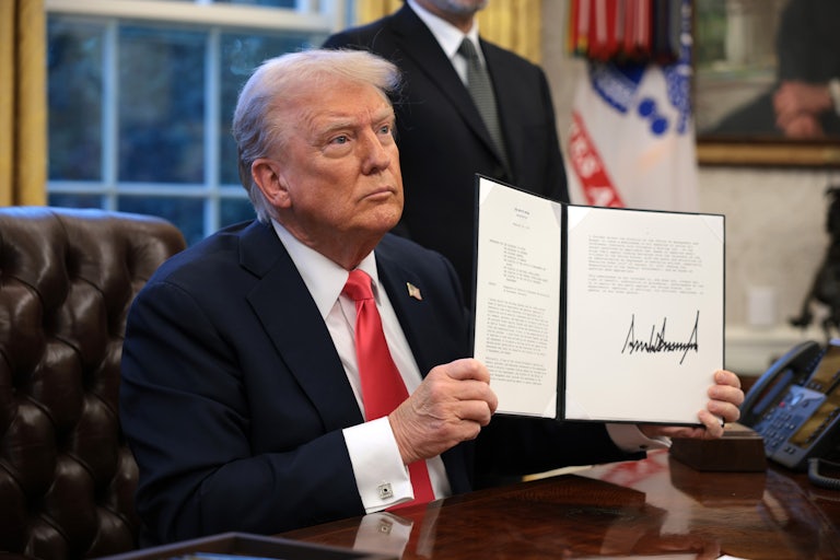 Donald Trump holds up a signed executive order while sitting in the Oval Office.