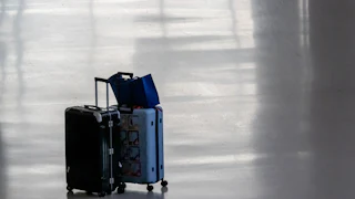 Two carry-on suitcases and a paper bag sit abandoned in an airport hall.