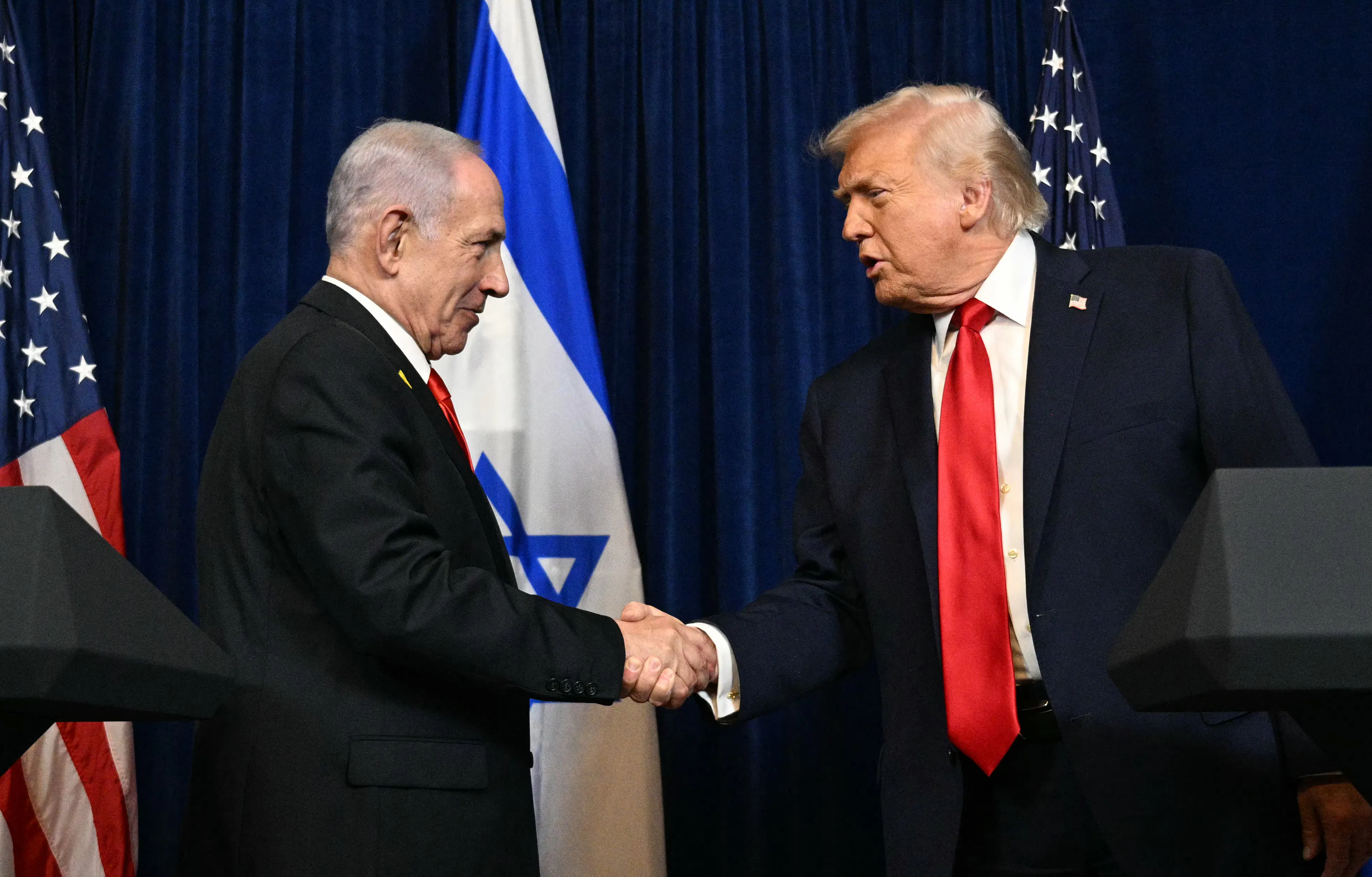 Israeli Prime Minister Benjamin Netanyahu and Donald Trump shake hands while standing at podiums during an event