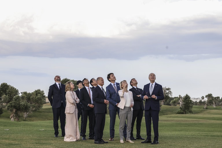 G7 leaders standing outside all tilt their heads back look up in the sky