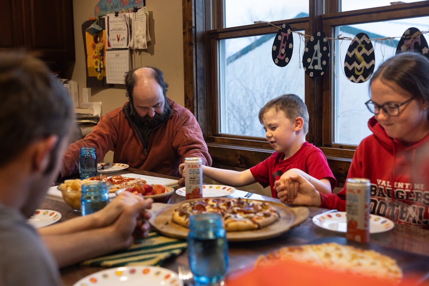 Four people hold hands around a dinner table in prayer. 