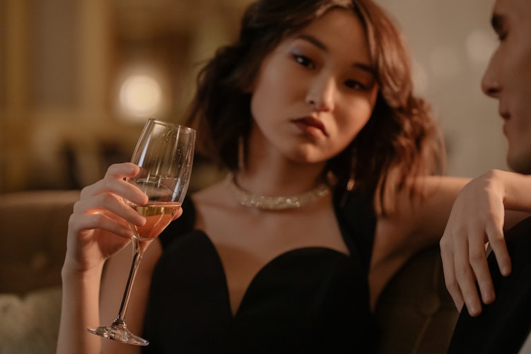 A woman holds a champagne flute and zones out while a man next to her talks to her.