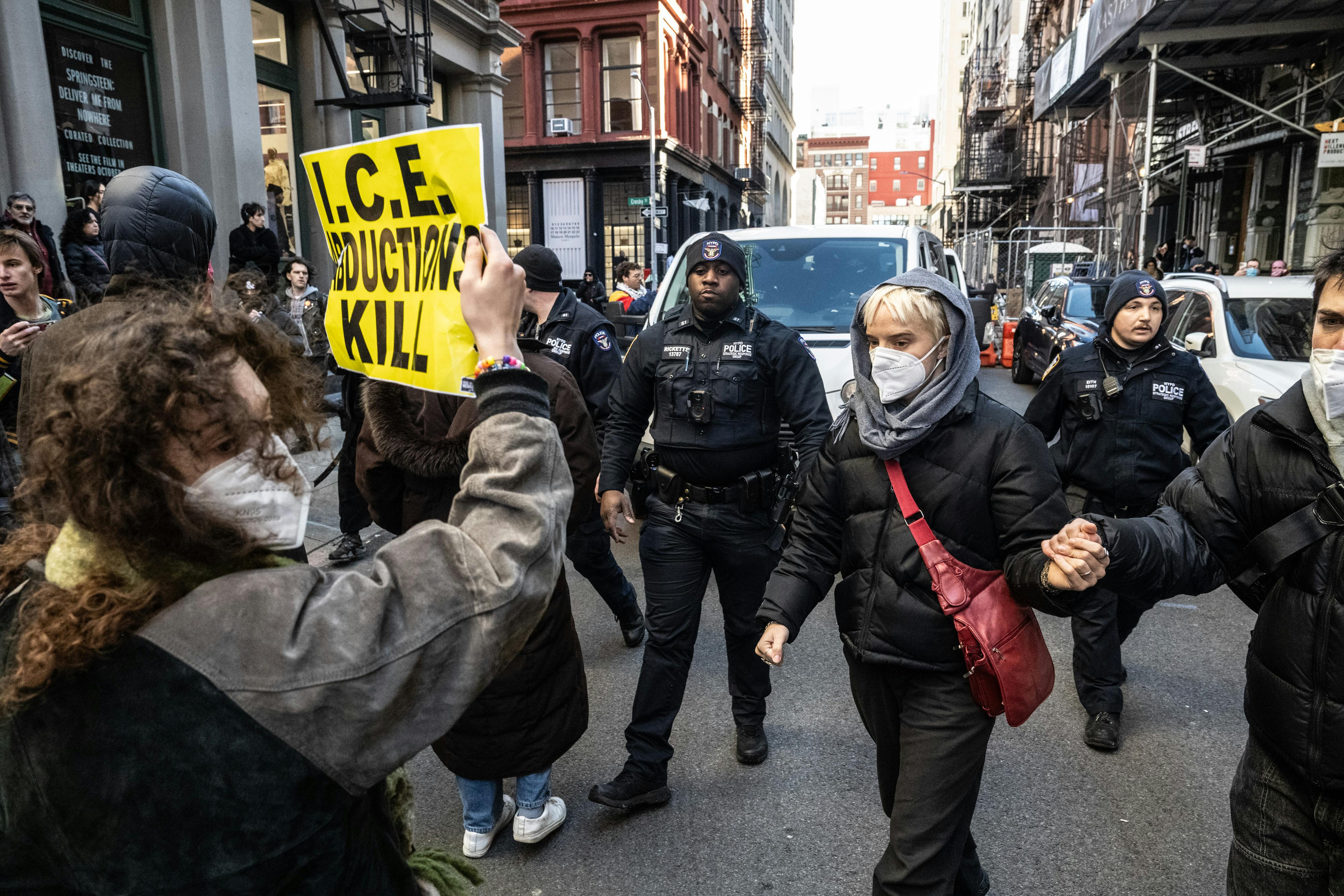 A protester holds up a sign reading "I.C.E. Abductions Kill" on Canal Street in New York City amidst other protesters and the NYPD.