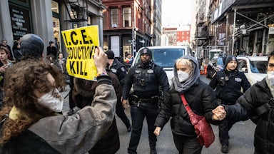 A protester holds up a sign reading "I.C.E. Abductions Kill" on Canal Street in New York City amidst other protesters and the NYPD.