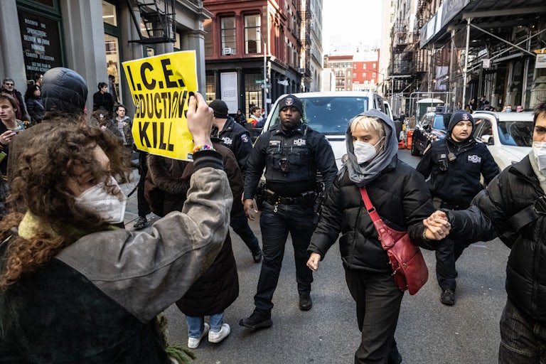 A protester holds up a sign reading "I.C.E. Abductions Kill" on Canal Street in New York City amidst other protesters and the NYPD.