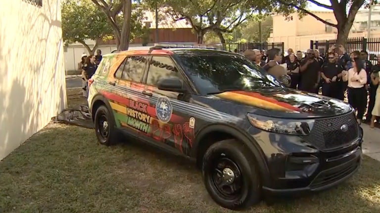 A black Miami police car painted in green, red, and yellow. On the side are the words "Black History Month" and several close fists raised in the air.
