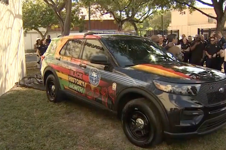 A black Miami police car painted in green, red, and yellow. On the side are the words "Black History Month" and several close fists raised in the air.