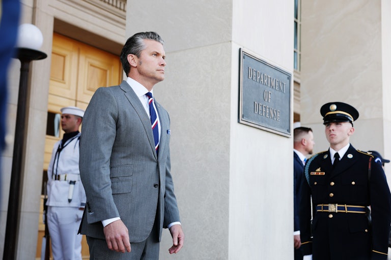Pete Hegseth stands outside the Pentagon, with a sign reading "Department of Defense."