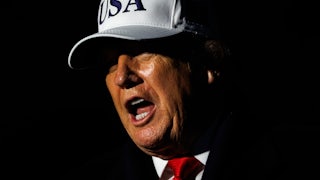Donald Trump speaks while wearing a white USA hat