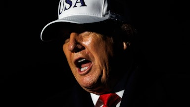 Donald Trump speaks while wearing a white USA hat