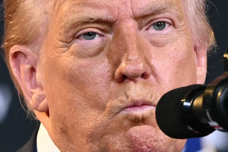Donald Trump purses his lips while standing at a microphone