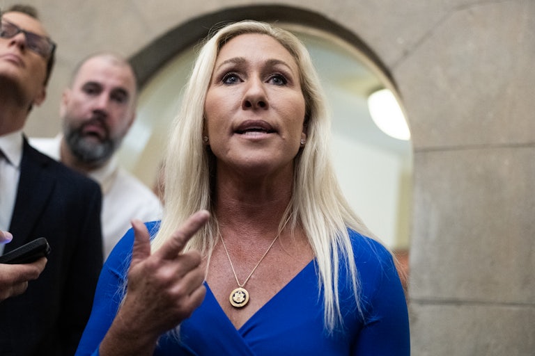 Representative Marjorie Taylor Greene speaks while pointing a finger angrily. Two reporters are in the background.