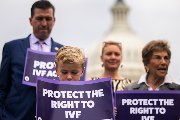 People standing outside the U.S. Capitol, including a young child, hold signs that read "Protect the Right to IVF."
