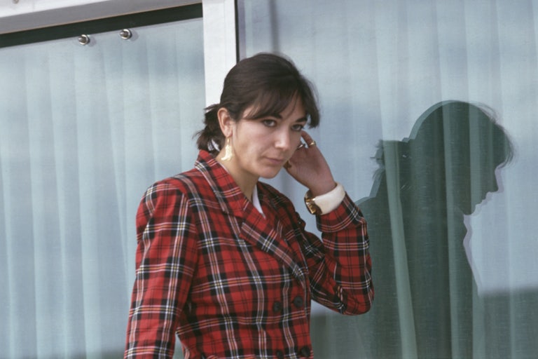Ghislaine Maxwell wears a plaid blazer and walks outside a curtained window.