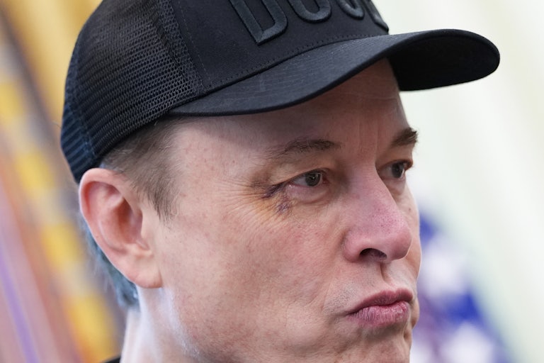Elon Musk purses his lips while wearing a DOGE cap.