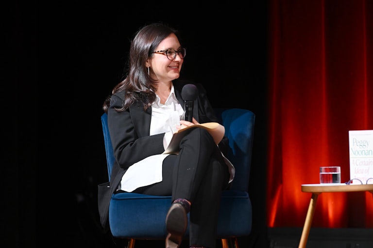 Bari Weiss crosses her legs as she sits on a chair on stage, talkign to someone else (unpictured).