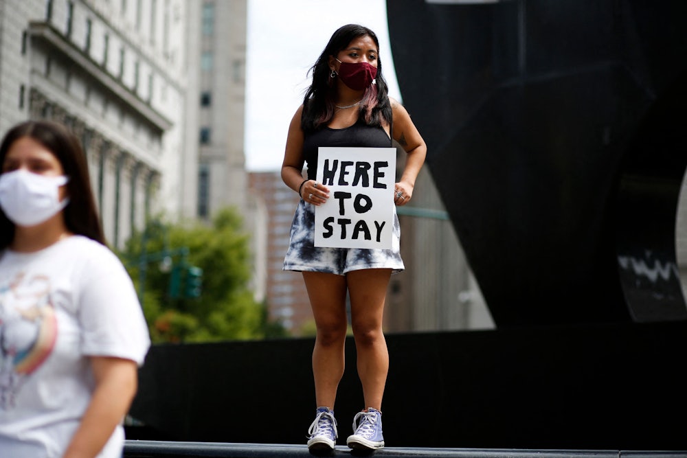 A young woman holds a banner reading “Here to Stay”