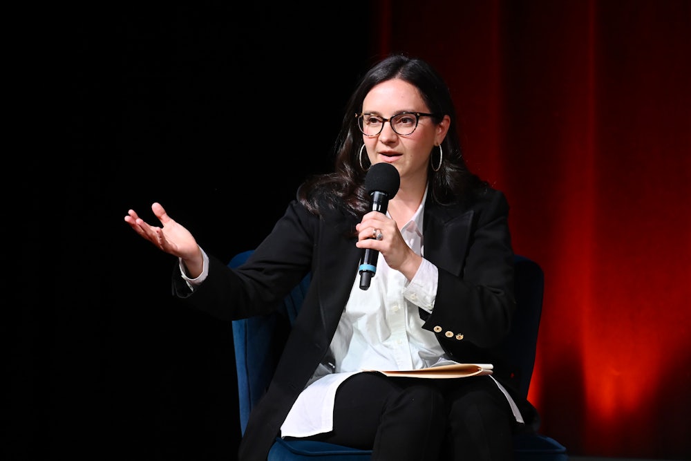 Bari Weiss gestures while speaking into a microphone while seated.