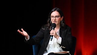 Bari Weiss gestures while speaking into a microphone while seated.