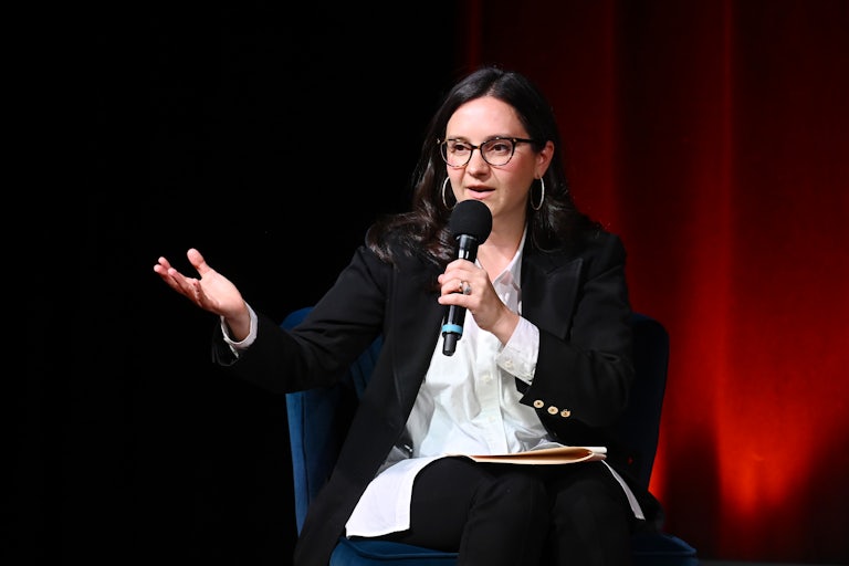 Bari Weiss gestures while speaking into a microphone while seated.