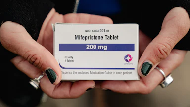 Hands with nail poish and rings holds a box of Mifepristone, 200 mg.