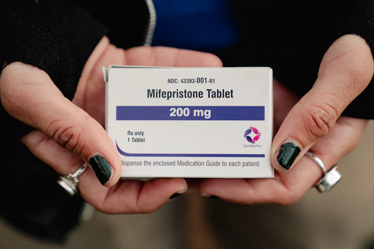 Hands with nail poish and rings holds a box of Mifepristone, 200 mg.