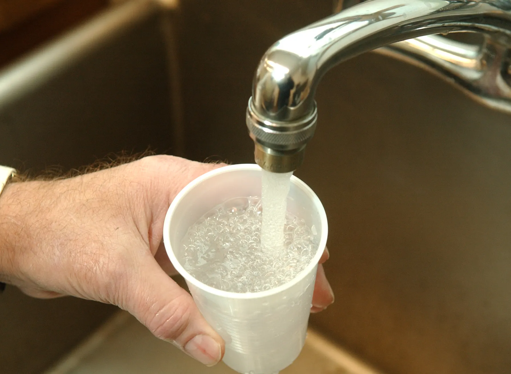 A hand holds a plastic cup under a running faucet.