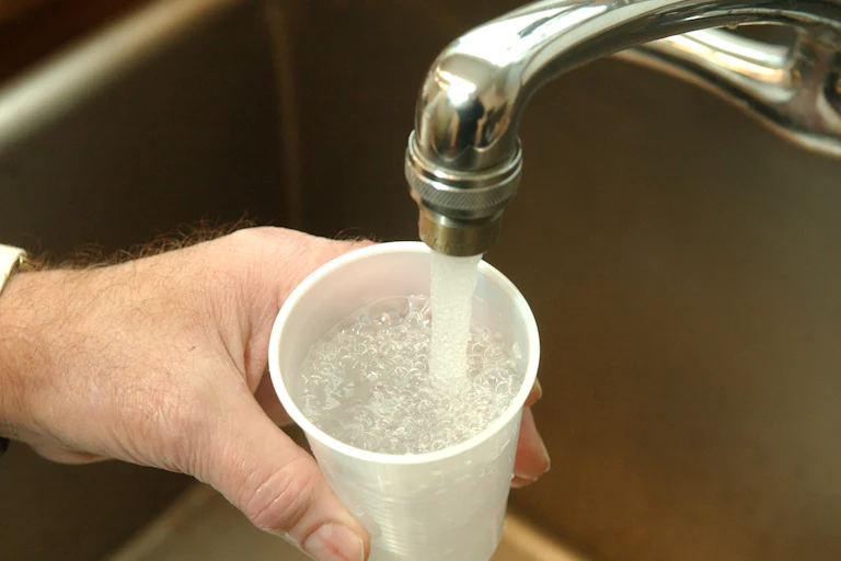 A hand holds a plastic cup under a running faucet.