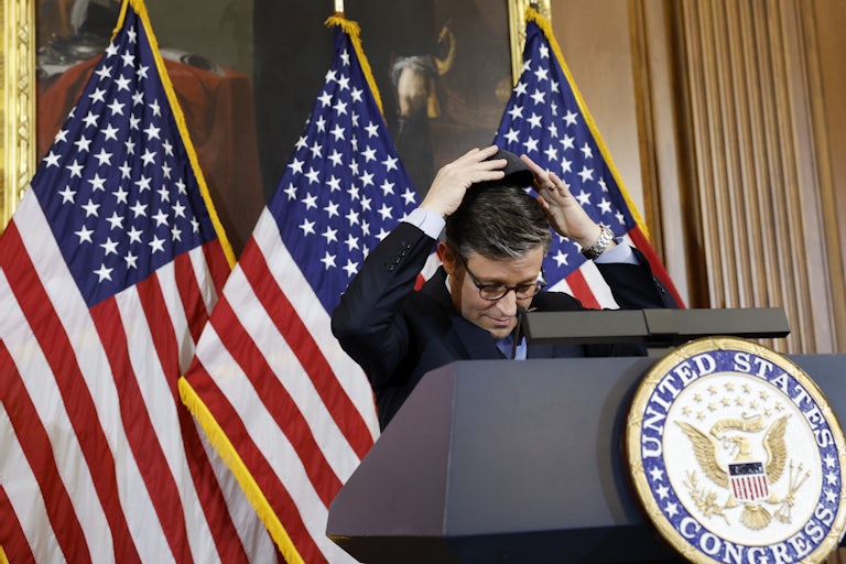 Mike Johnson puts his hands on his head as he stands at a lectern