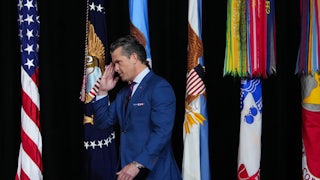 Defense Secretary Pete Hegseth salutes s he walks in front of several flags.
