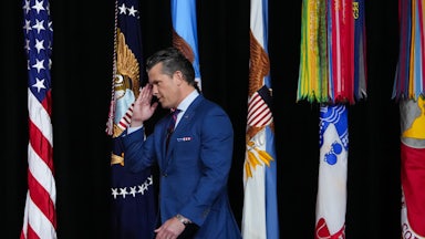 Defense Secretary Pete Hegseth salutes s he walks in front of several flags.