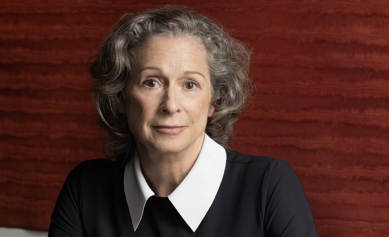 Heiress Abigail Disney, dressed elegantly in black, photographed sitting in front of a red contemporary art work  at her dining room table in her home in New York City.  