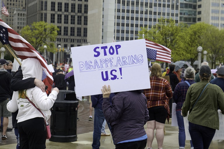 A protester holds a sign that reads "Stop disappearing us."