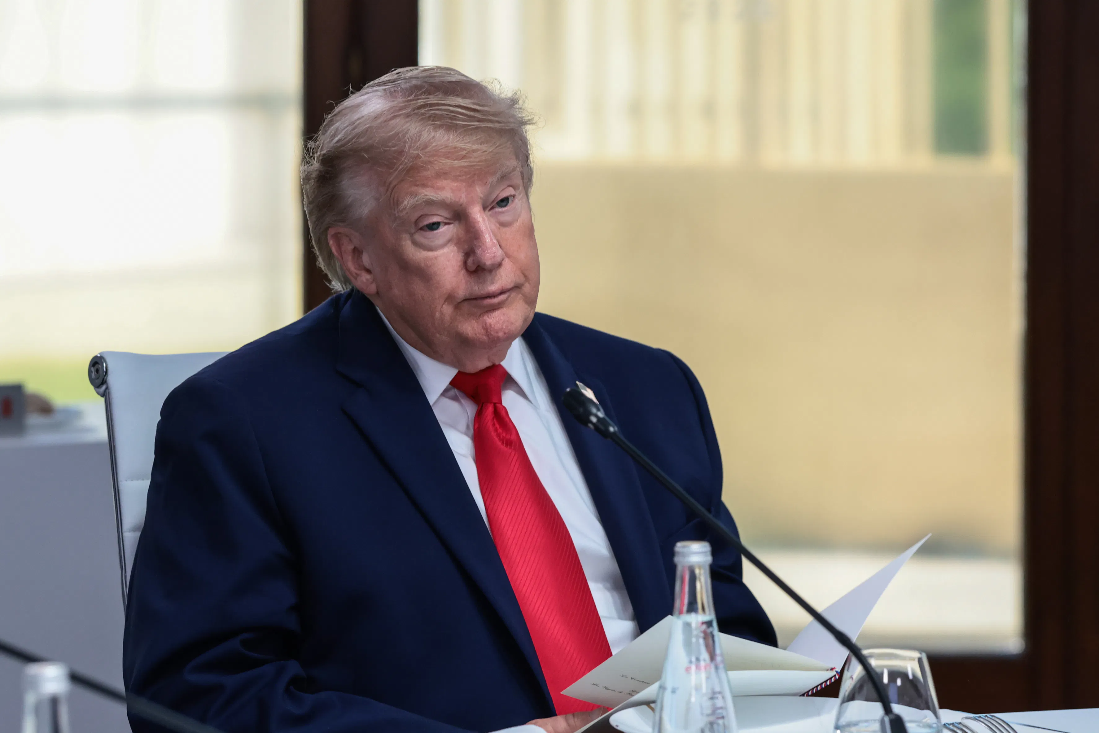 A fatigued Donald Trump, sitting down wearing a blue suit and red tie.