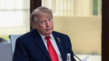 A fatigued Donald Trump, sitting down wearing a blue suit and red tie.
