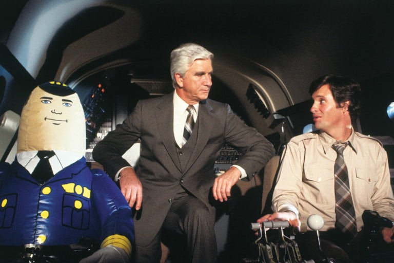 Actors Leslie Nielson and Robert Hays sit next to an inflatable pilot.