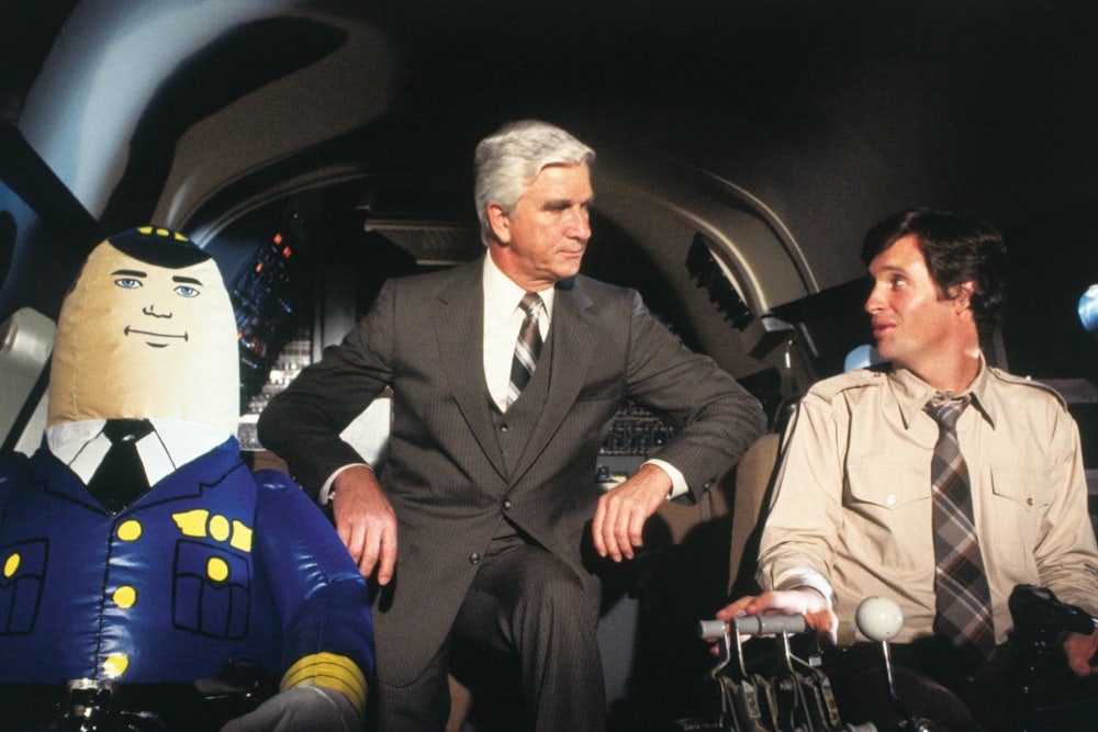 Actors Leslie Nielson and Robert Hays sit next to an inflatable pilot.