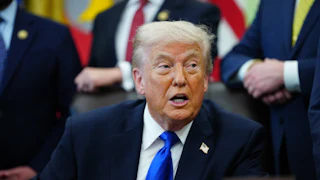 Donald Trump turns to the side and speaks while sitting at his desk in the Oval Office
