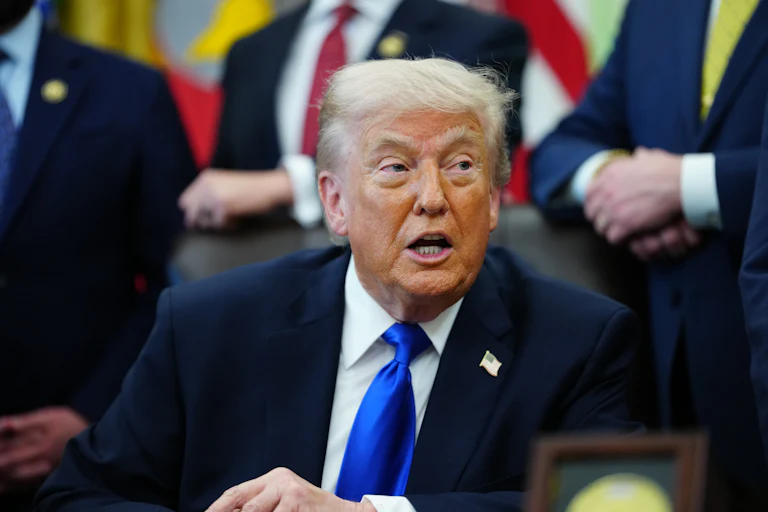 Donald Trump turns to the side and speaks while sitting at his desk in the Oval Office