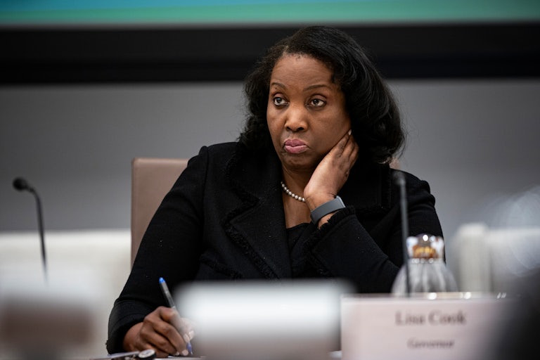 Federal Reserve Governor Lisa Cook puts her hand on the side of her neck while sitting at a table