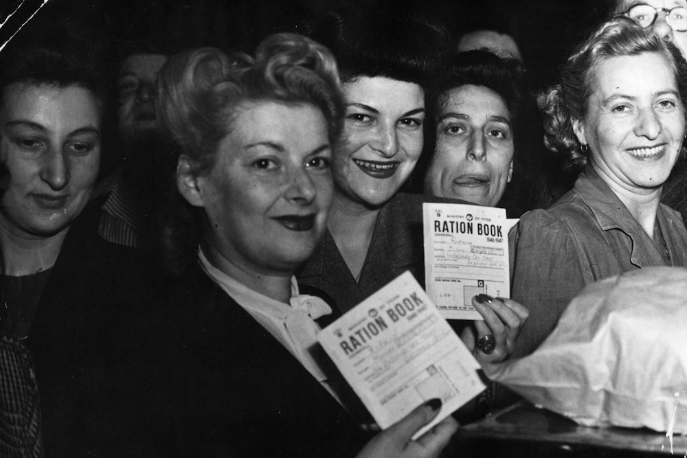 Women hold up their ration books while smiling.